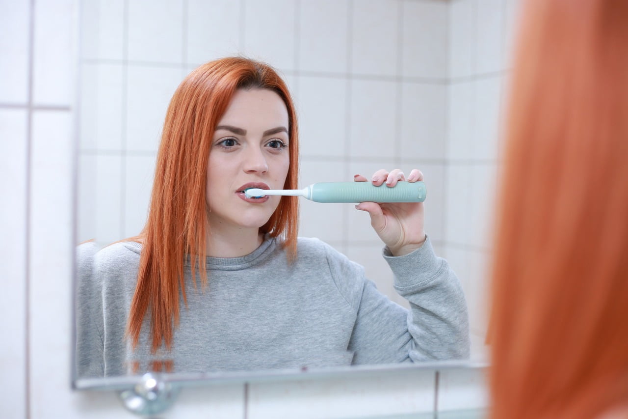 Red Hair Women Brushing Her Teeth in Front of Mirror